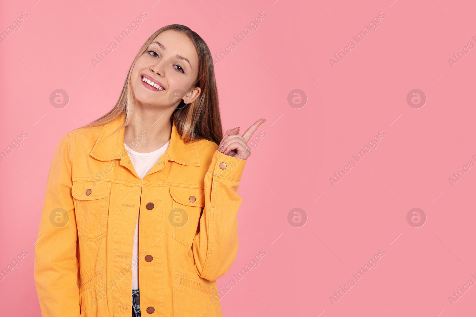 Photo of Beautiful teenage girl pointing at something on pink background. Space for text