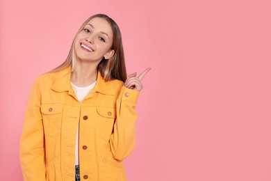 Beautiful teenage girl pointing at something on pink background. Space for text