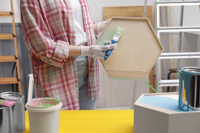 Photo of Woman painting honeycomb shaped shelf with brush indoors, closeup