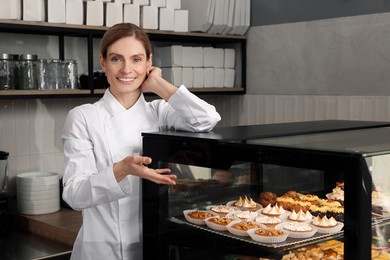 Professional baker near showcase with pastries in store