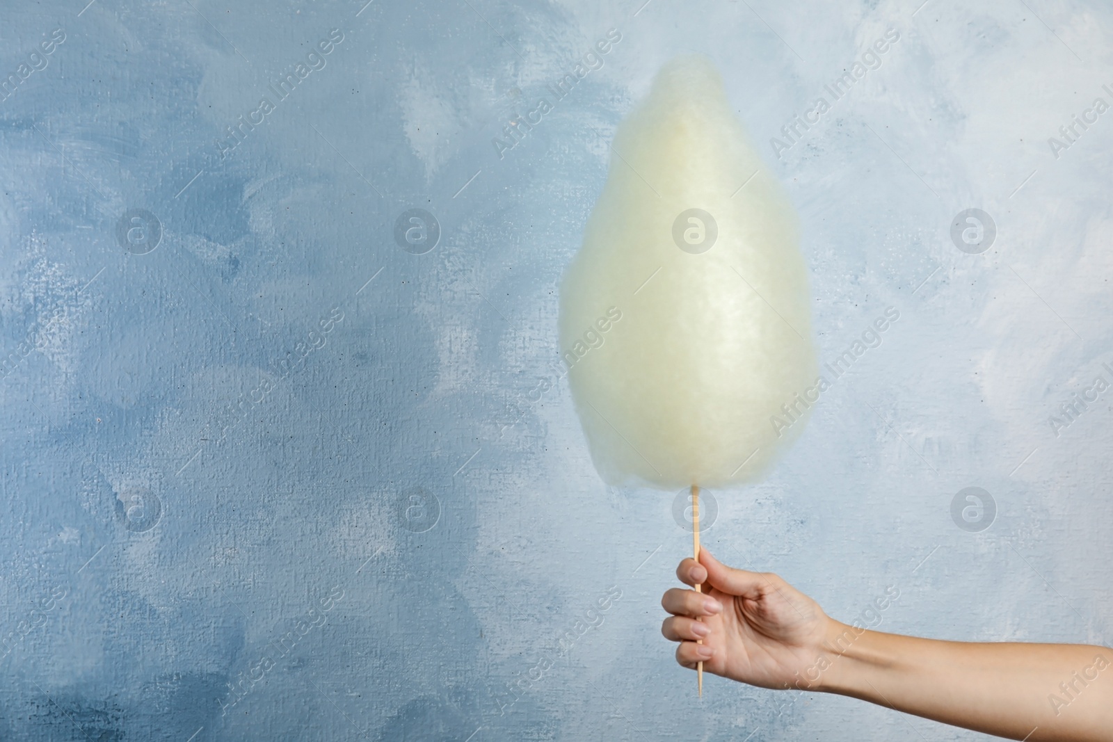 Photo of Woman holding sweet cotton candy on light blue background, closeup view. Space for text