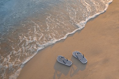 Striped beach slippers on sand near sea, above view. Space for text