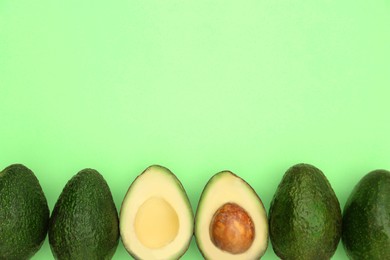 Photo of Tasty whole and cut avocados on light green background, flat lay. Space for text