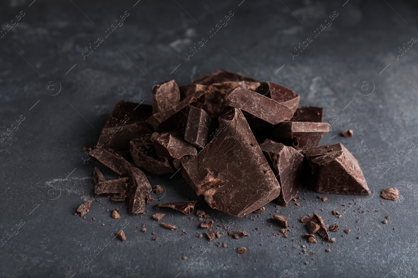 Photo of Pieces of tasty dark chocolate on grey table, closeup