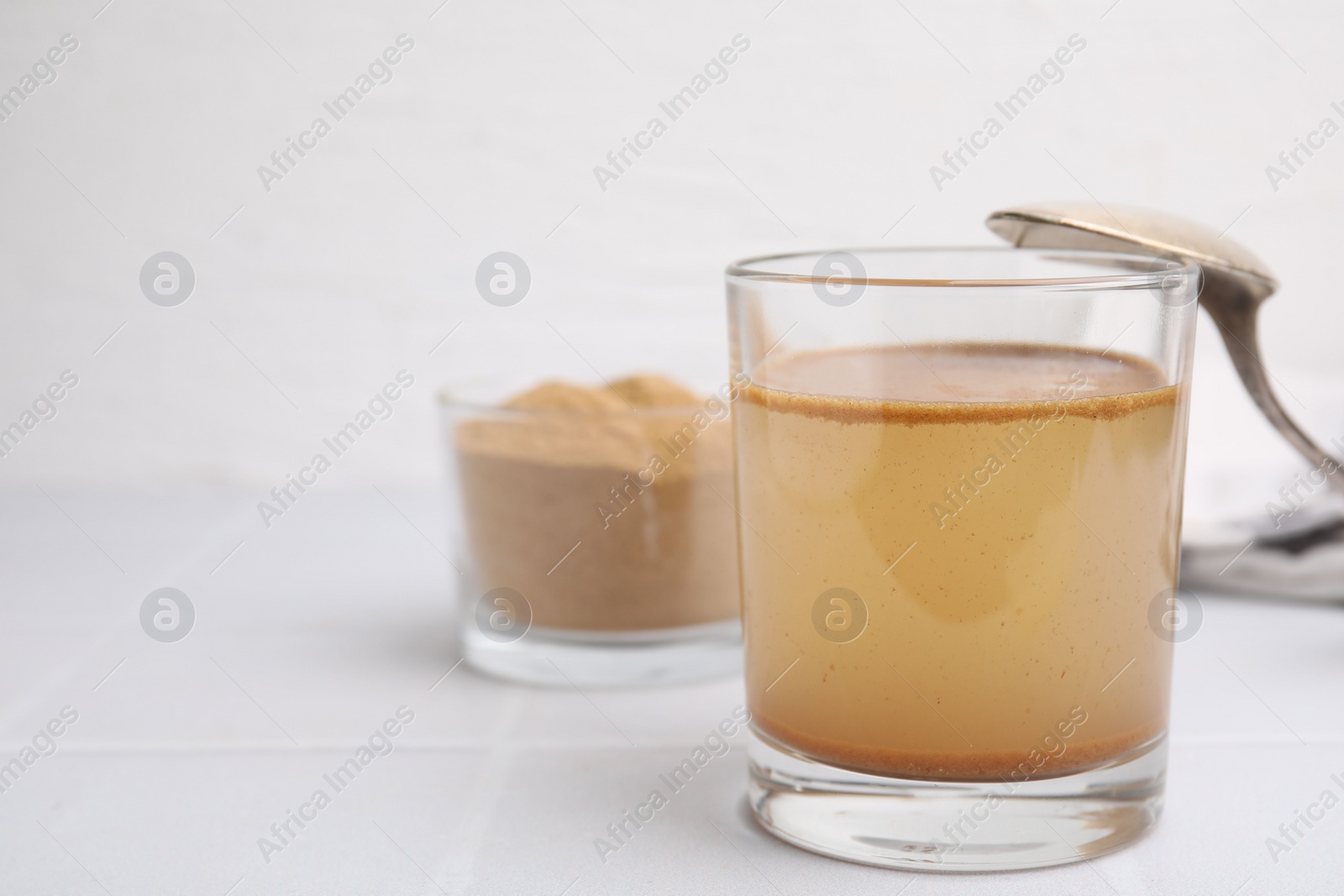 Photo of Soluble fiber with water in glass and powder on white tiled table, space for text