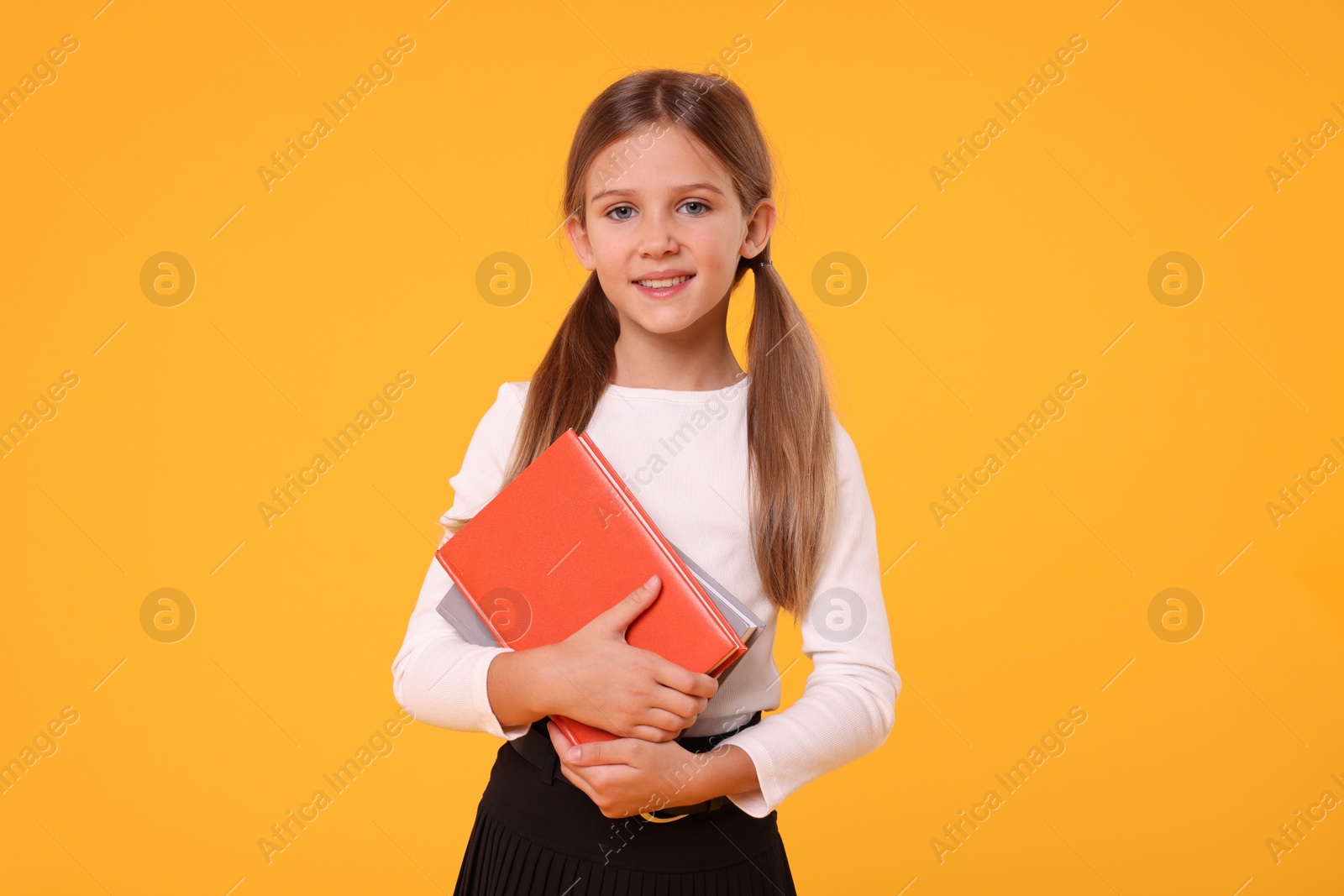 Photo of Happy schoolgirl with books on orange background