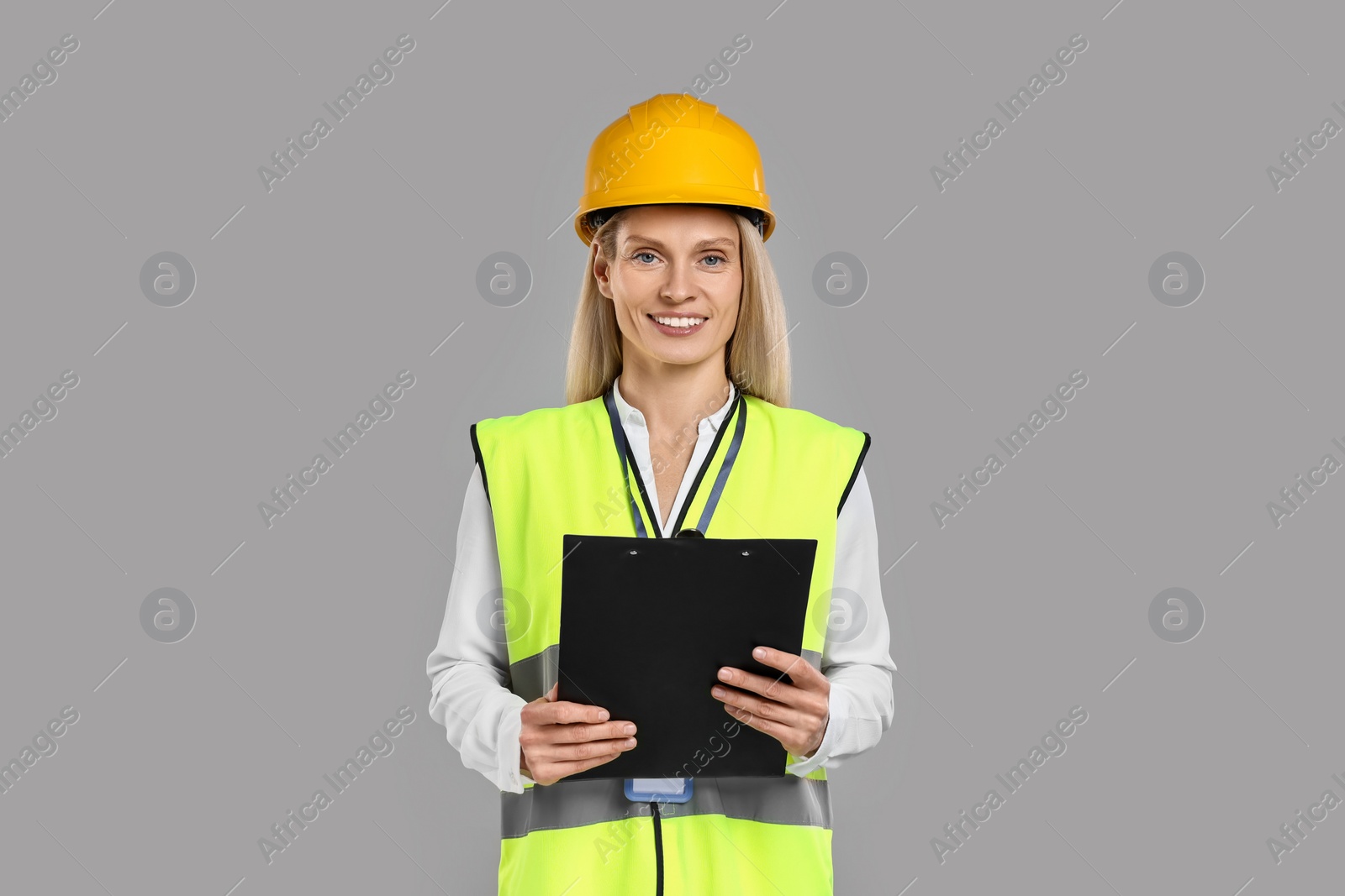 Photo of Engineer in hard hat holding clipboard on grey background