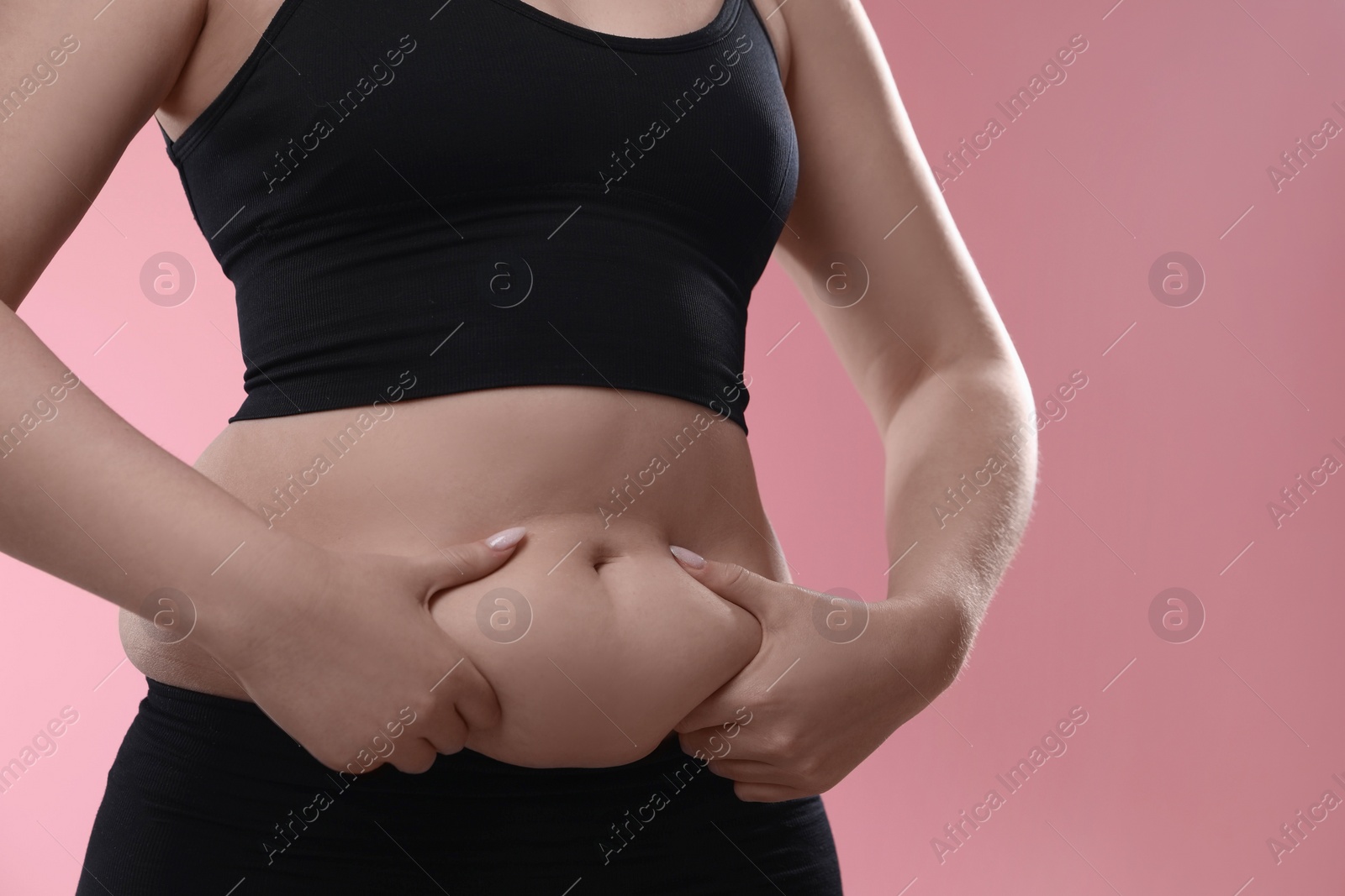 Photo of Woman touching belly fat on pink background, closeup. Overweight problem