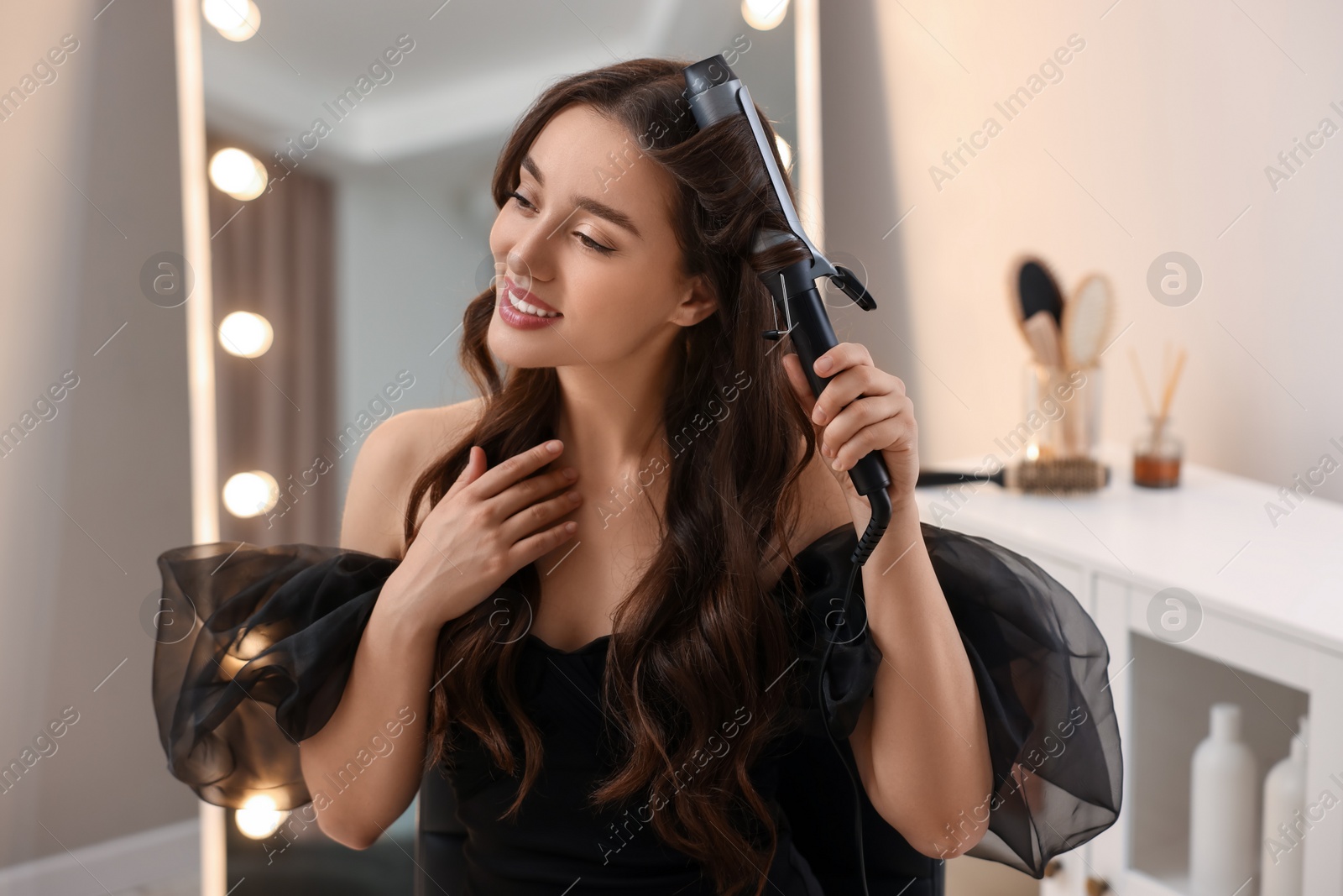 Photo of Smiling woman using curling hair iron at home