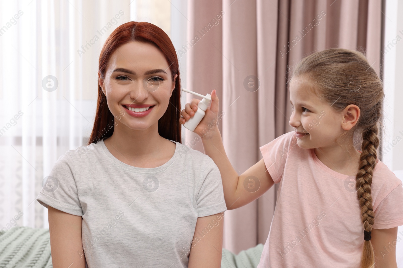 Photo of Little girl spraying medication into mother's ear at home