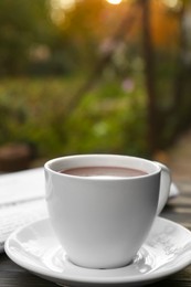 Photo of White cup with coffee and newspaper on table, closeup. Morning ritual
