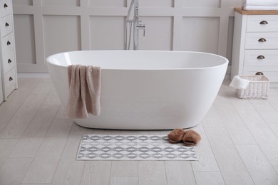 Photo of Stylish mat and slippers on floor near tub in bathroom. Interior design