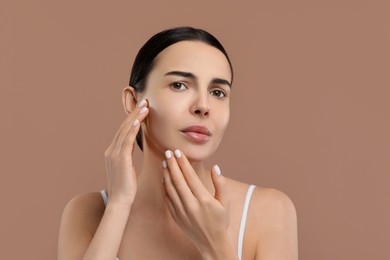 Woman with dry skin checking her face on beige background, space for text