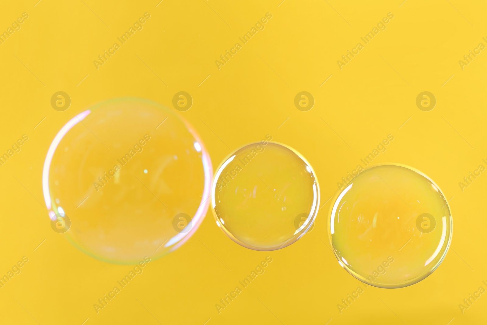 Photo of Beautiful transparent soap bubbles on yellow background