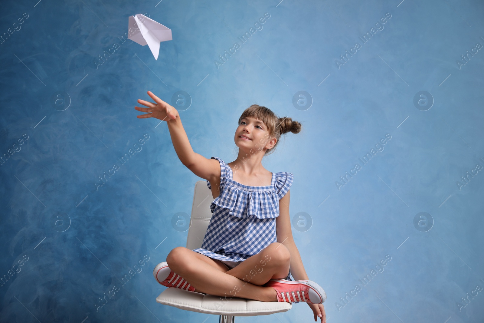 Photo of Cute little girl playing with paper plane on light blue background