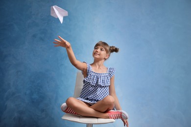 Photo of Cute little girl playing with paper plane on light blue background