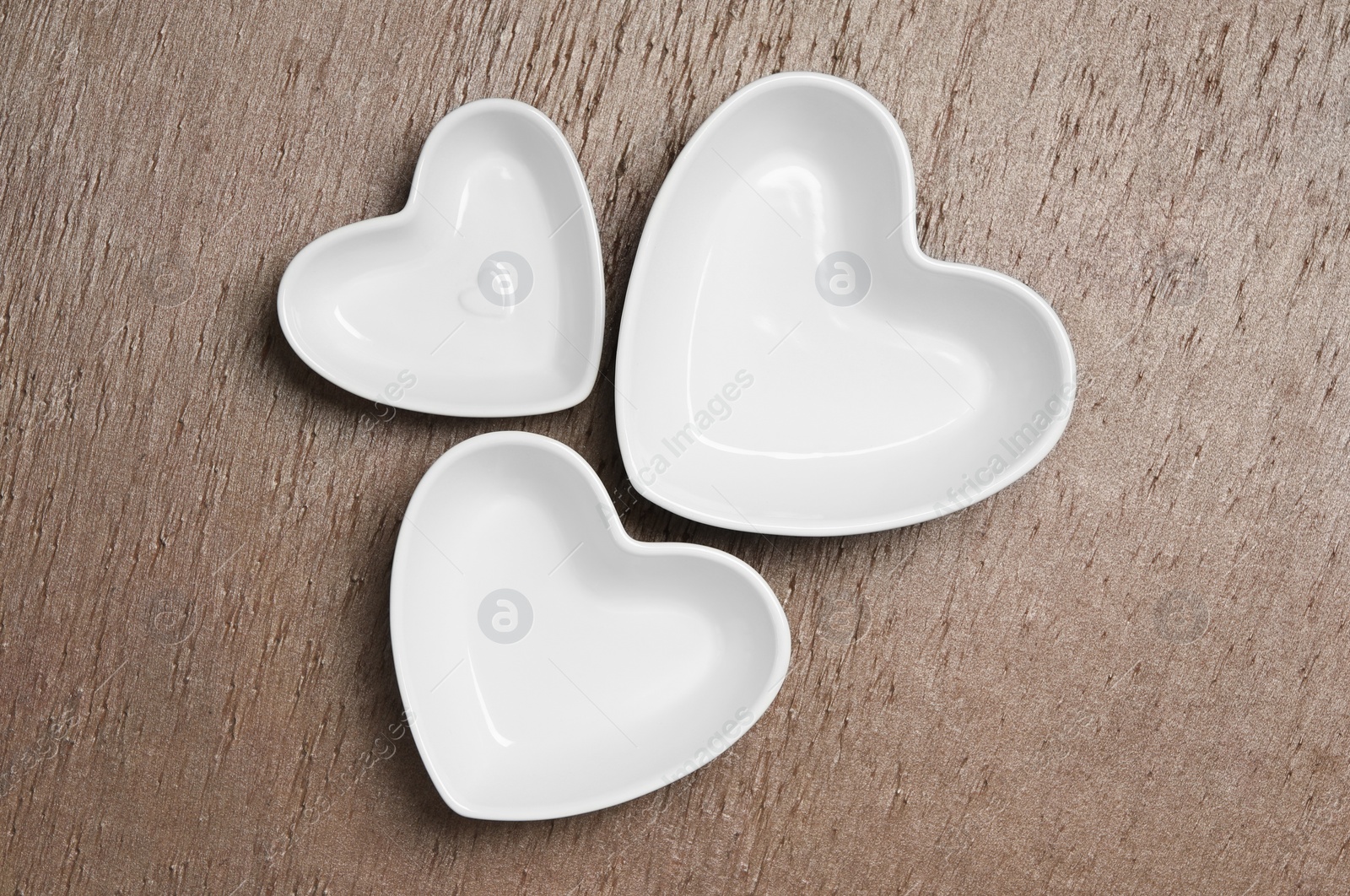 Photo of Heart shaped baking dishes on wooden table, flat lay. Cooking utensils