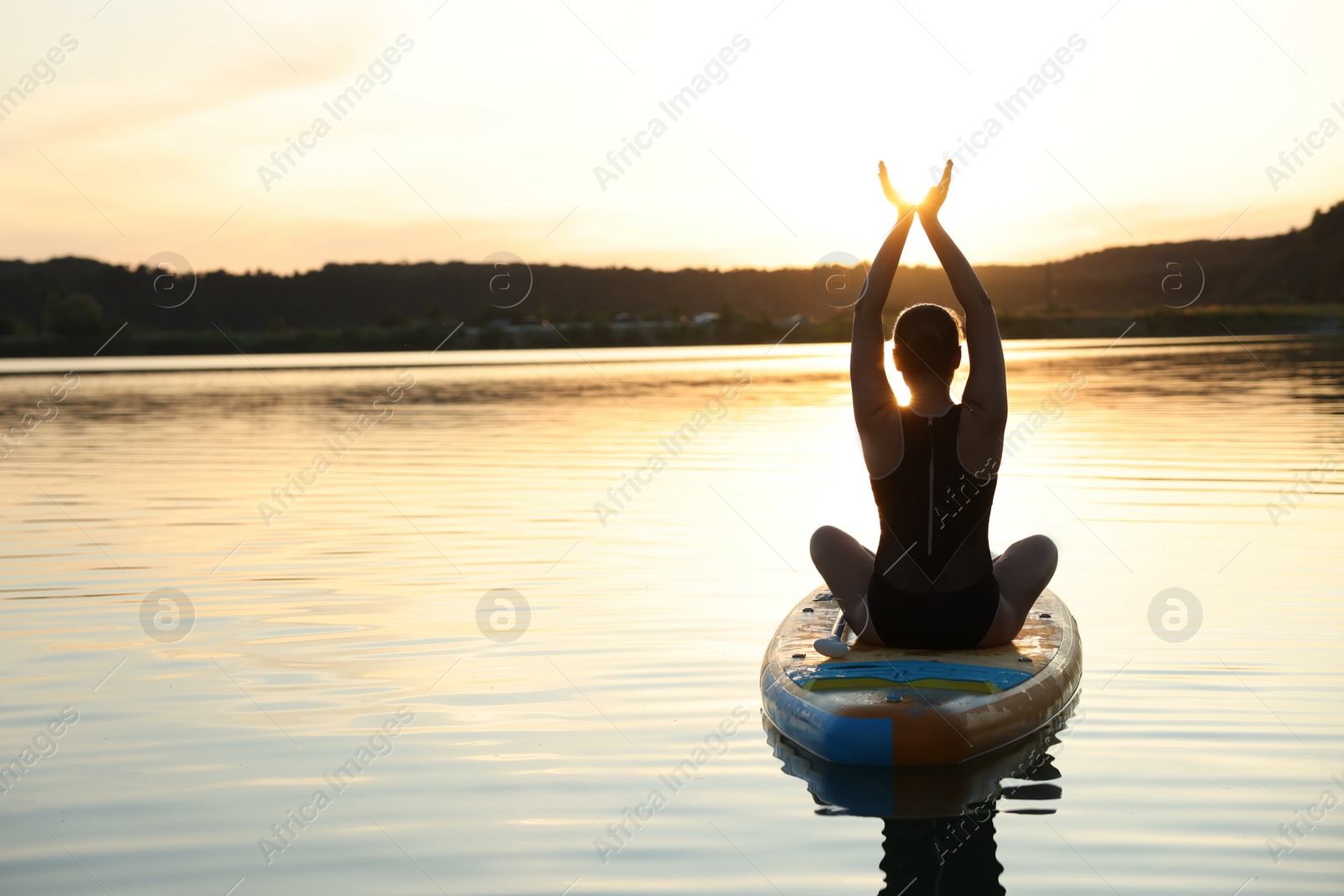 Photo of Woman practicing yoga on SUP board on river at sunset, back view