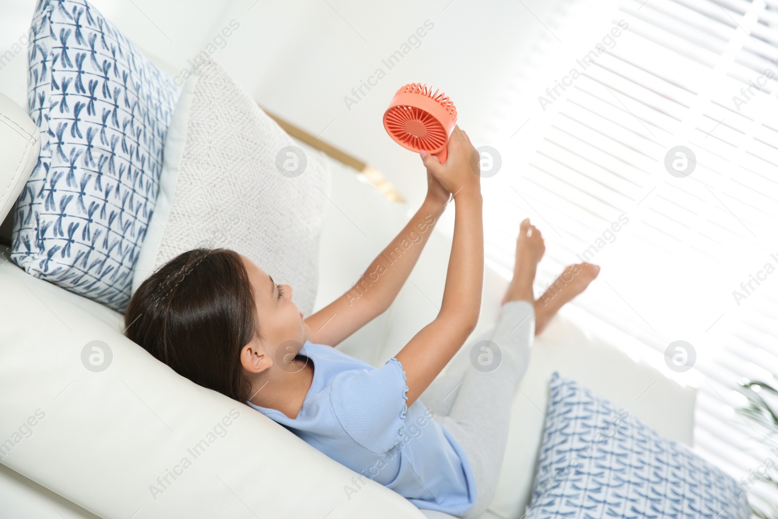 Photo of Little girl with portable fan at home. Summer heat