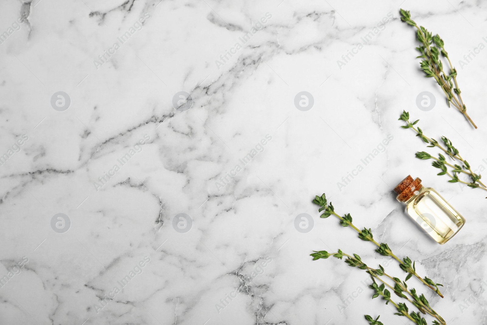 Photo of Essential oil in glass bottle, thyme and space for text on marble background, flat lay