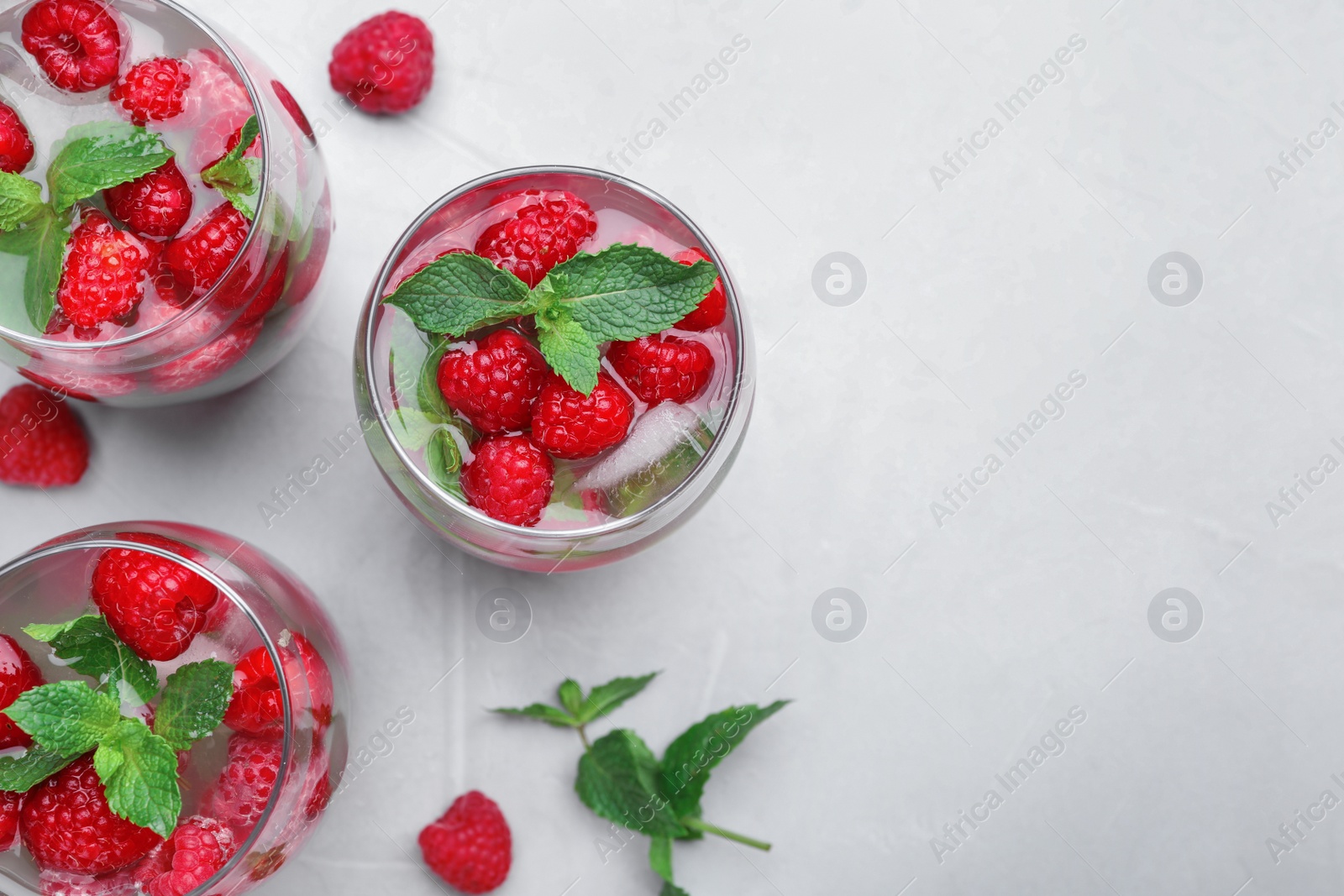 Photo of Glasses of refreshing drink with raspberry and mint on grey stone table, flat lay. Space for text