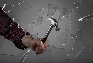 Image of Man breaking window with hammer on dark grey background, closeup