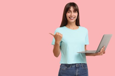 Special promotion. Happy woman with laptop pointing at something on pink background, space for text