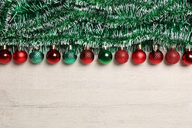 Photo of Green tinsel and Christmas balls on white wooden background, flat lay. Space for text