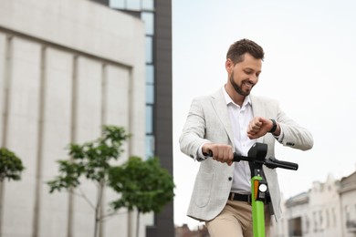 Businessman with modern kick scooter on city street, space for text