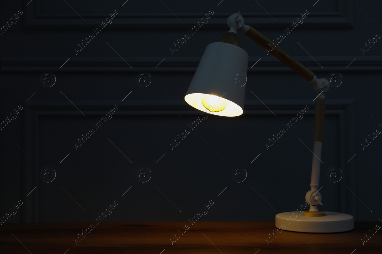 Photo of Stylish modern desk lamp on wooden table at night, space for text