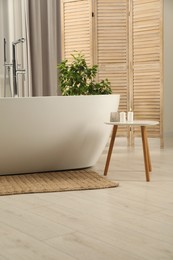 Photo of Spa day. Stylish bathroom with ceramic tub, houseplant and wooden side table