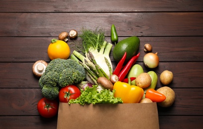 Fresh vegetables in paper shopping bag on wooden table, flat lay