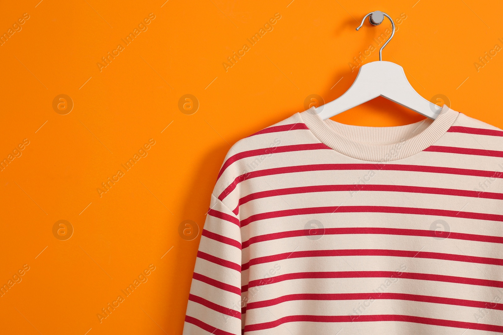 Photo of Hanger with striped sweatshirt on orange wall, space for text