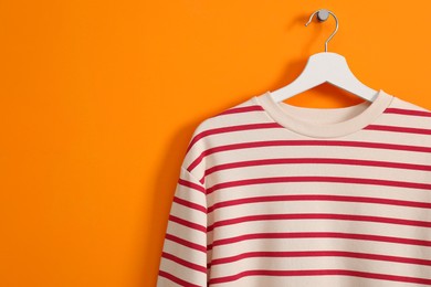 Photo of Hanger with striped sweatshirt on orange wall, space for text