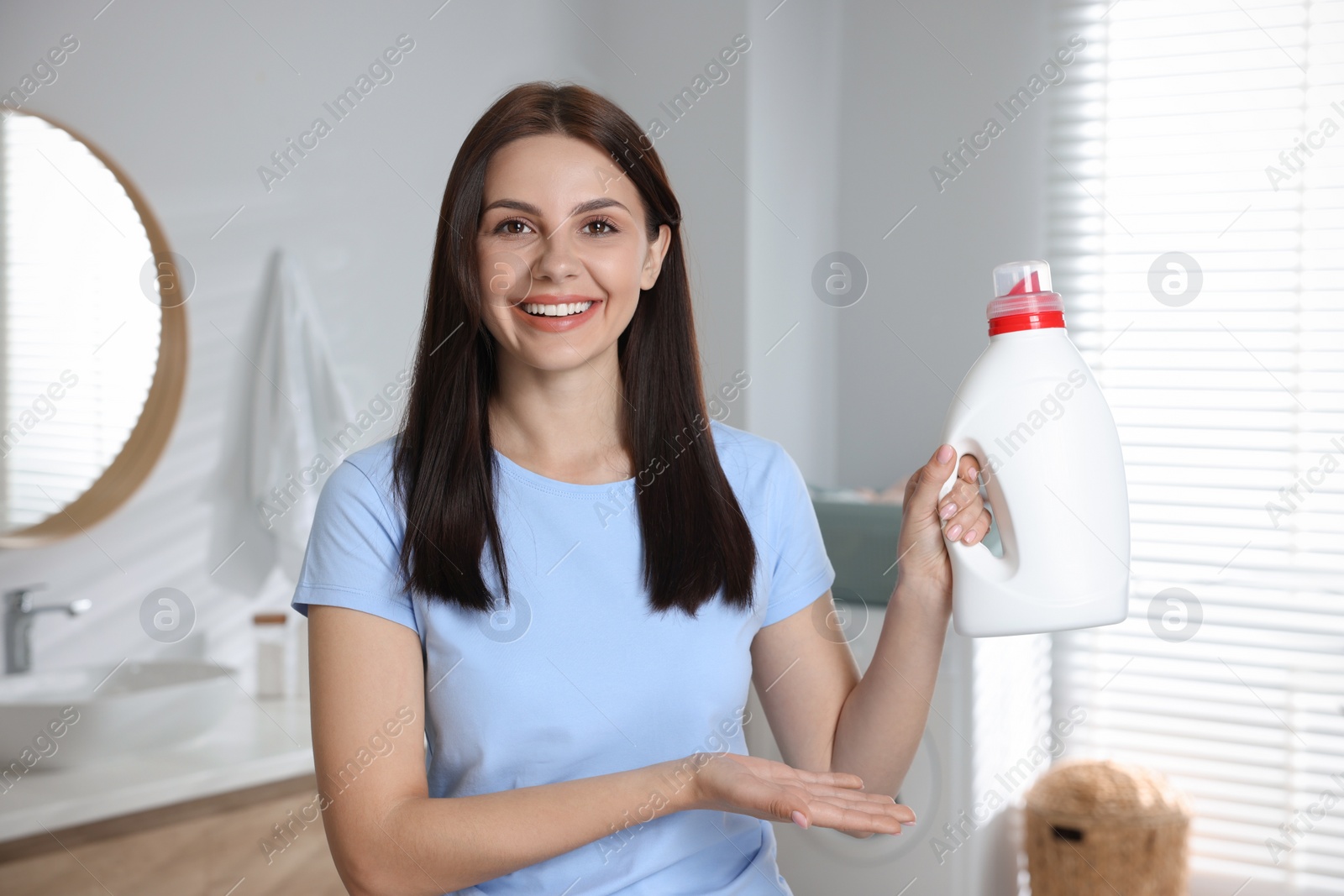 Photo of Beautiful woman showing fabric softener in bathroom