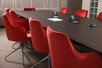 Photo of Stylish red office chairs and large wooden table in empty conference room