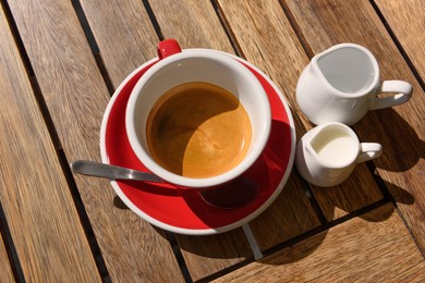 Photo of Cup of aromatic hot coffee, milk and water on wooden table, above view