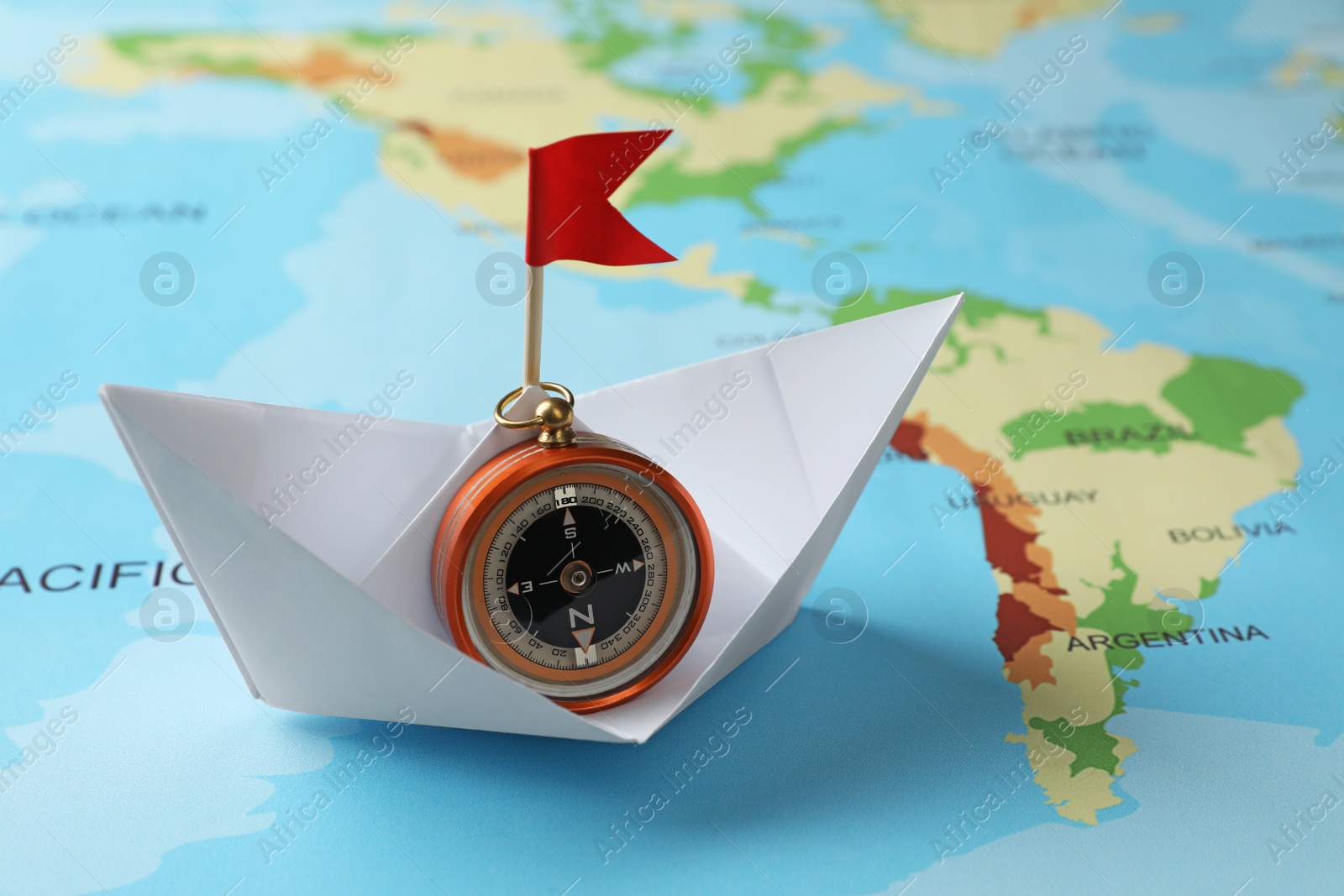 Photo of White paper boat with compass on world map