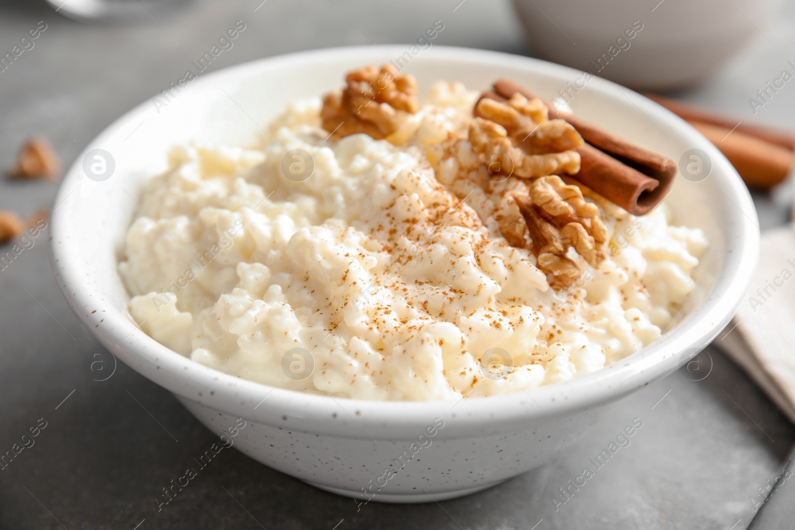 Photo of Creamy rice pudding with cinnamon and walnuts in bowl on grey table