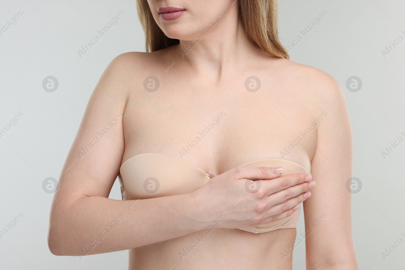 Photo of Mammology. Young woman doing breast self-examination on light grey background, closeup