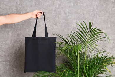 Young man holding eco bag at indoor palm plant near grey wall