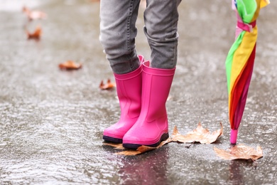 Little girl with rubber boots and umbrella after rain, focus of legs. Autumn walk
