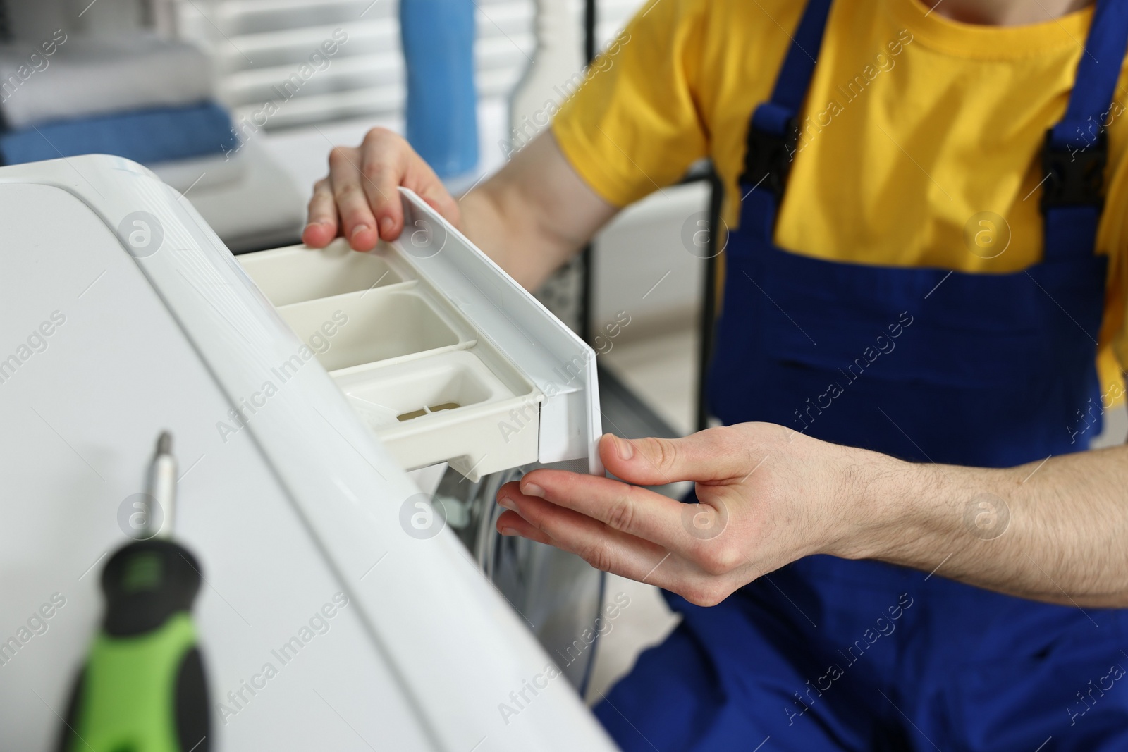 Photo of Plumber pulling detergent drawer out of washing machine indoors, closeup