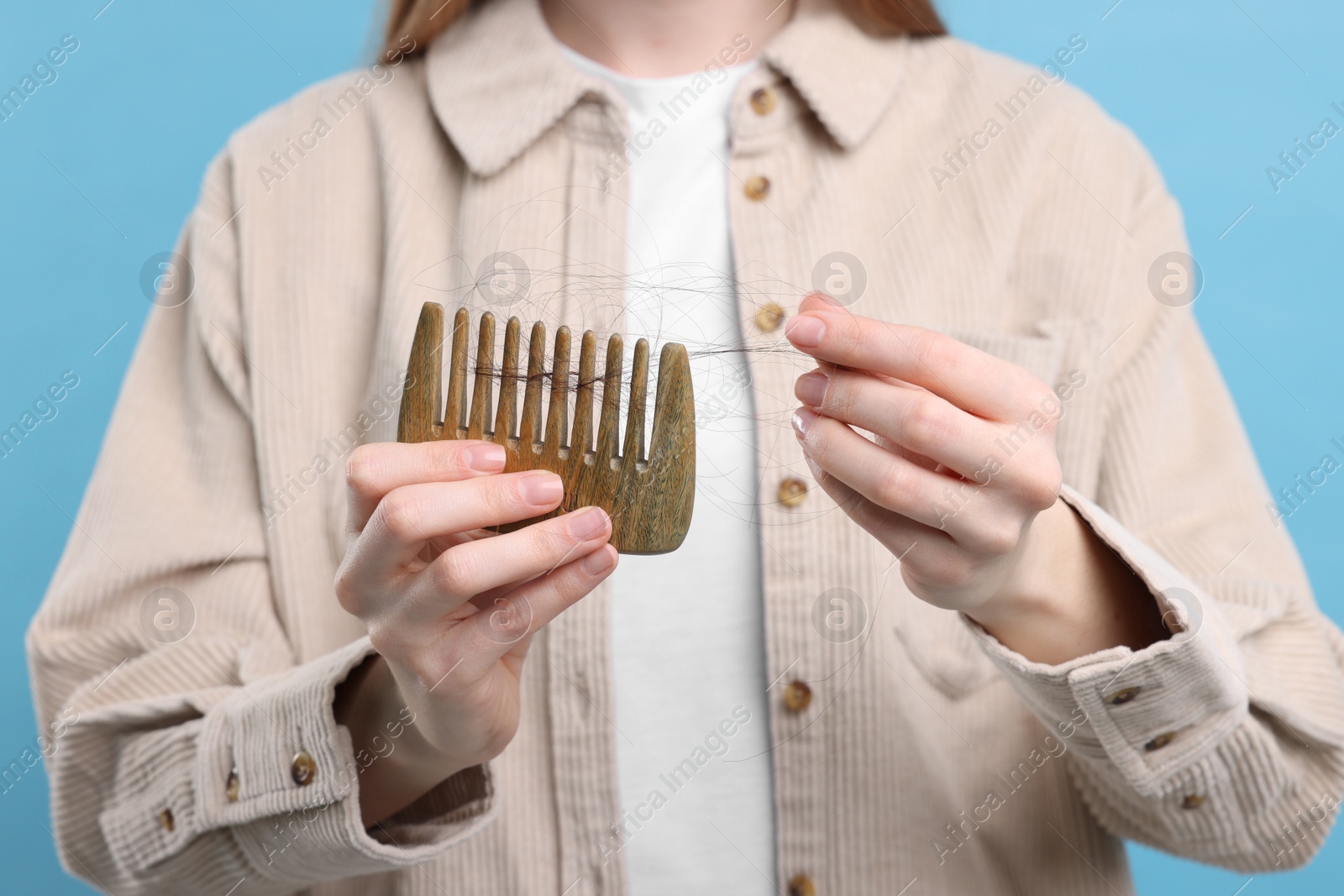 Photo of Woman holding comb with lost hair on light blue background, closeup. Alopecia problem