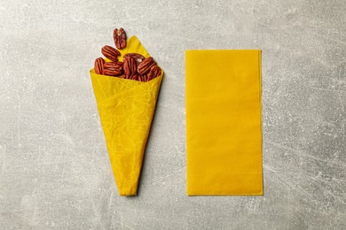 Photo of Yellow reusable beeswax food wraps with nuts on grey table, flat lay
