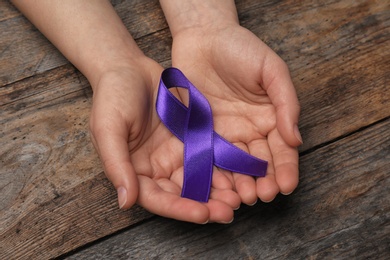 Woman with purple awareness ribbon on wooden background, closeup