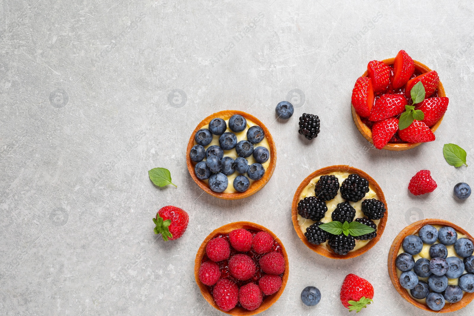 Photo of Tartlets with different fresh berries on light grey table, flat lay and space for text. Delicious dessert