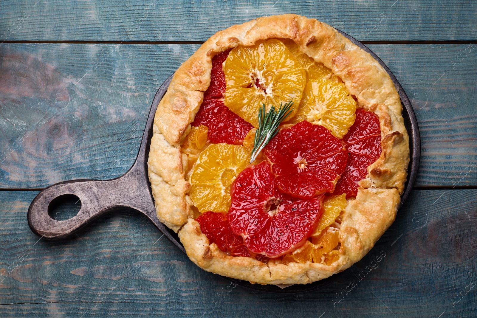 Photo of Delicious galette with citrus fruits and rosemary on blue wooden table, top view