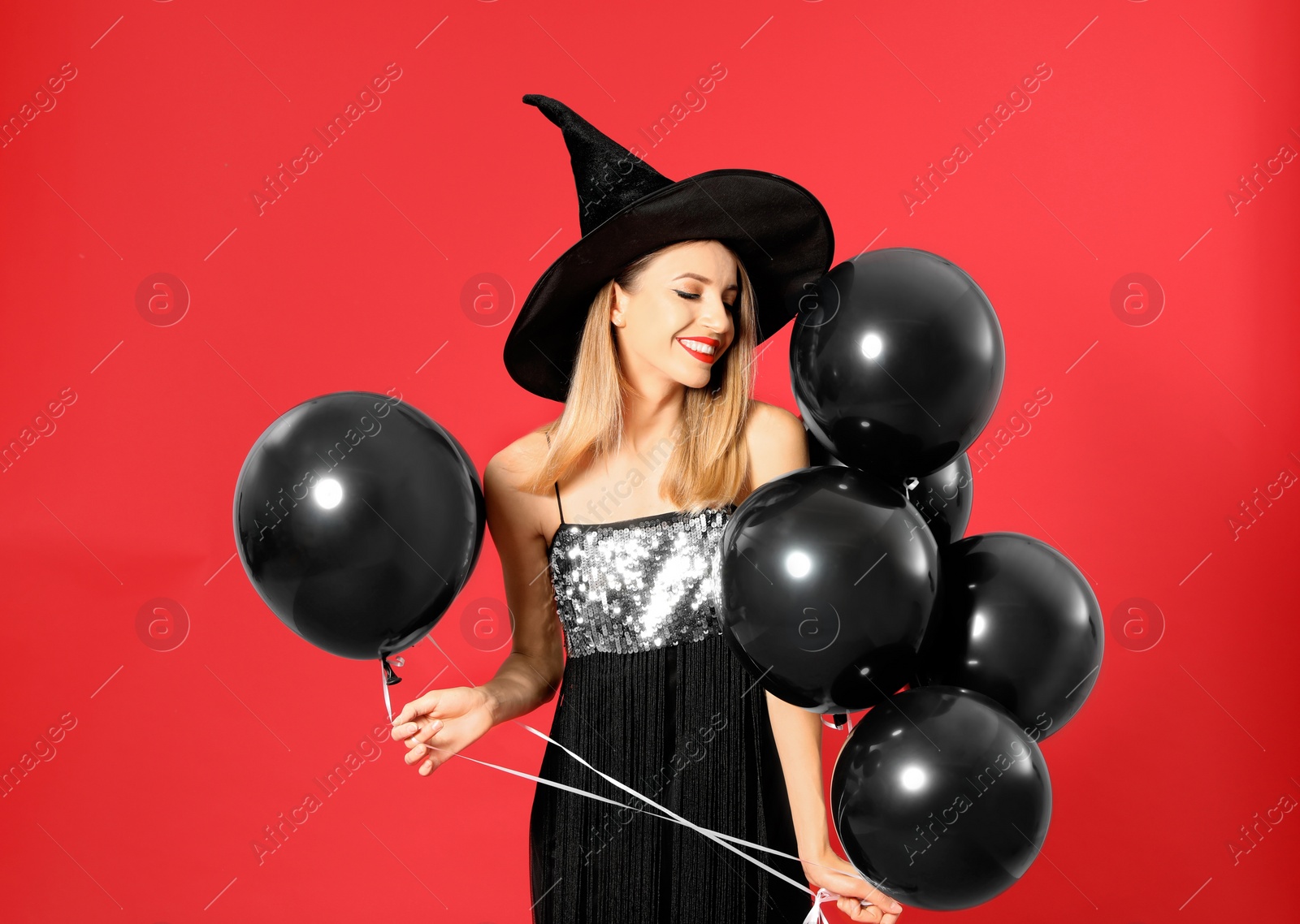 Photo of Beautiful woman wearing witch costume with balloons for Halloween party on red background