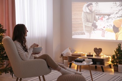 Photo of Woman with popcorn watching romantic Christmas movie via video projector at home